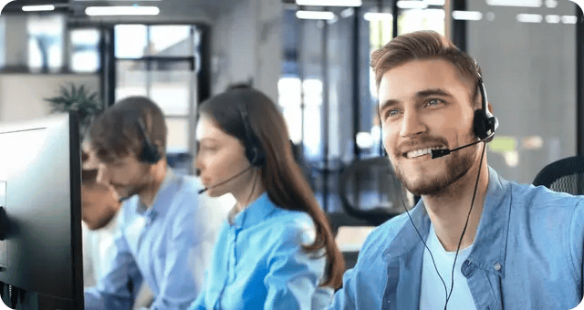 3 Personen mit Headsets sitzen vor Monitoren und lächeln