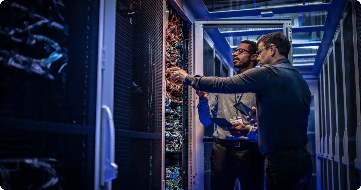 Zwei Männer stehen vor einem Server und kontrollieren die Verkabelung