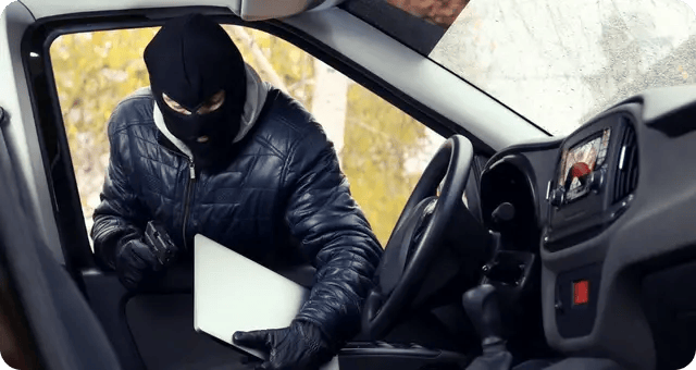 Ein Dieb klaut einen Laptop aus einem Auto