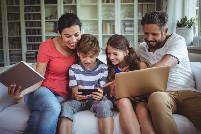 Happy family sitting on sofa and using laptop, mobile phone and digital tablet at home-1